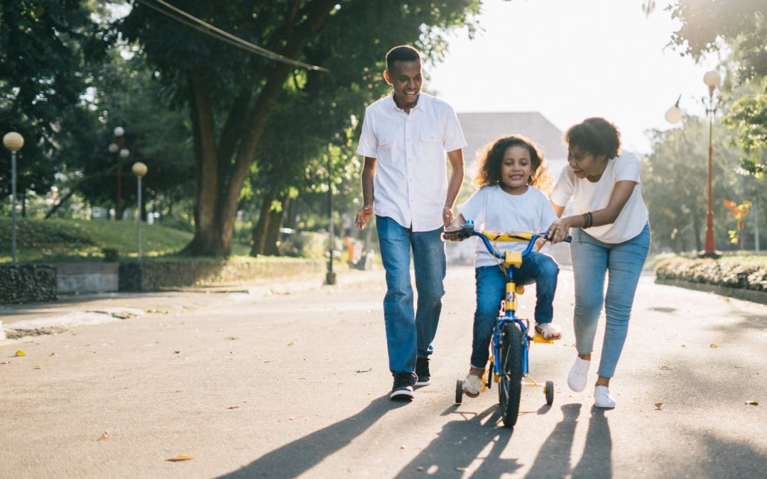 A man standing beside his wife teaching their child how to ride bicycle representing the need for effective co-parenting and the benefits of High Conflict Divorce and Family Reunification Services.