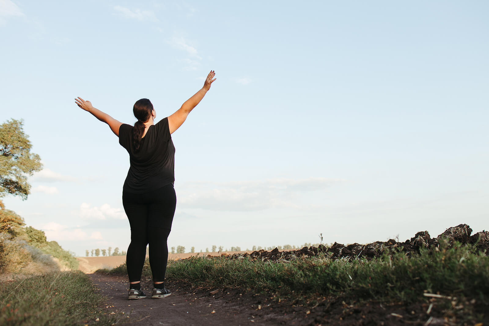 Curvy woman standing with her arms raised above her head in celebration of her successful mental health journey. You relationship with food and your size do not define you as a person. Learn to restore and recover with binge eating treatment in Los Angeles, CA.