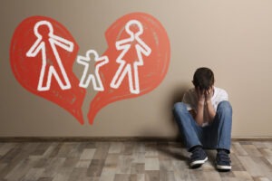 Child sitting on the floor with their head in their hands with a broken heart drawn on the wall representing the impact of divorce on children. High Conflict Divorce and Family Reunification Services can help.