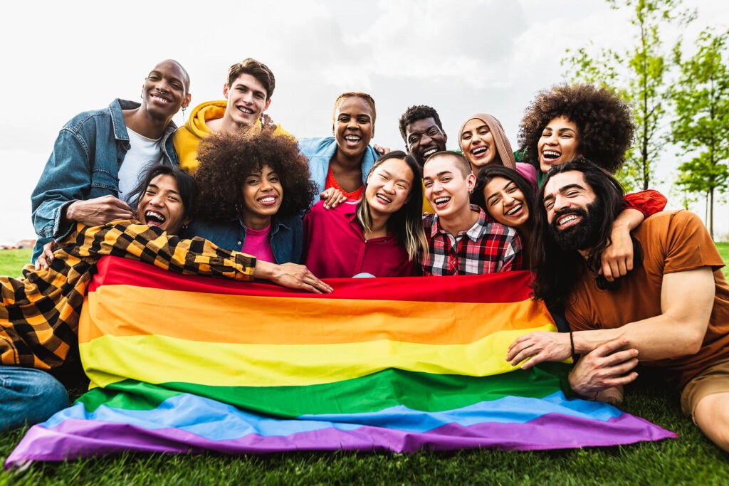 Group of LGBTQ adults sitting together and supporting each other while holding a pride flag representing the sense of belonging and care that can come from working with LGBTQ Affirming Therapy in Los Angeles, CA.